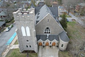 Gothic Revival church with crenellated tower, rose window, and triple-arched entrance in residential setting.