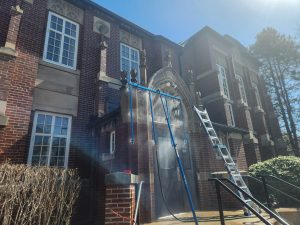 Maintenance work at arched doorway with blue scaffolding and water spray, ladder leaning against brick facade.