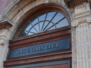 Arched wooden entrance to Boys & Girls Club building with address 277, set in carved stone facade.