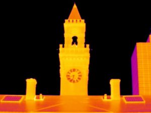 Thermal image of clock tower showing warm yellow-orange heat signatures against black sky background.